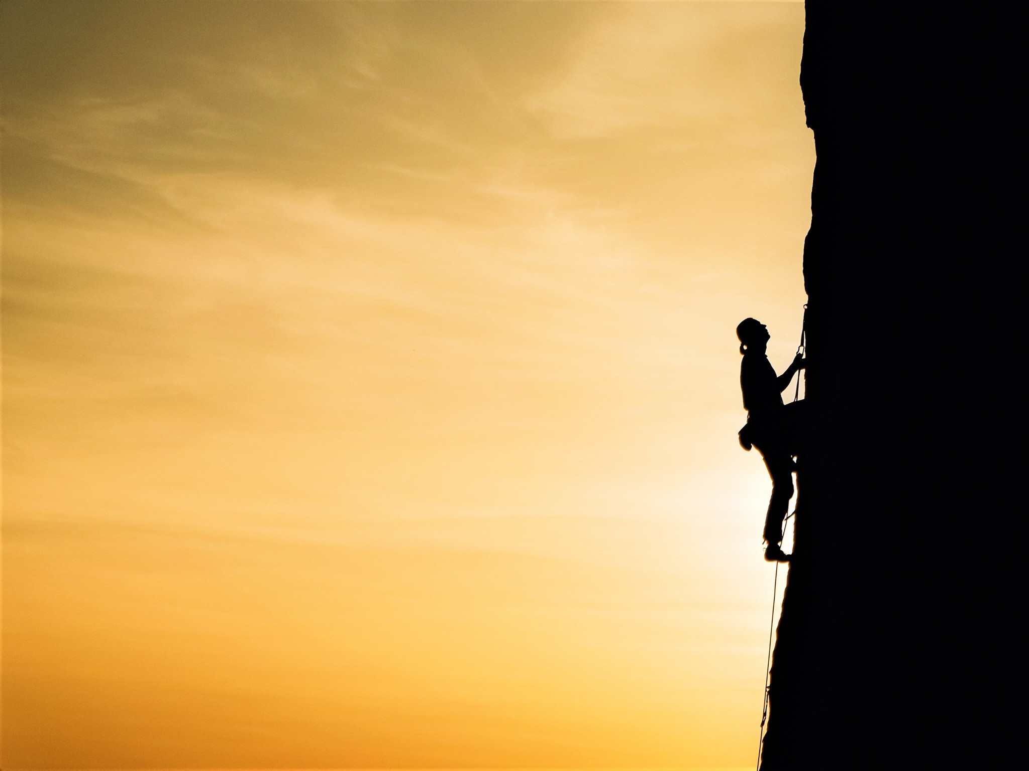 A silhouetted man scaling a vertical cliff during twilight.